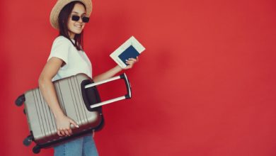 happy female traveler with suitcase on red background