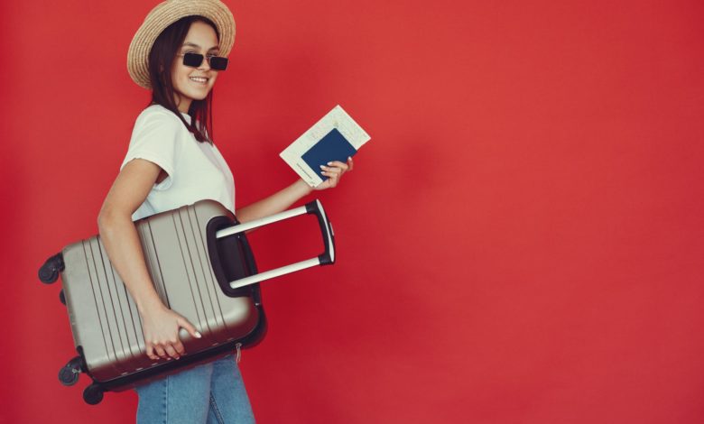 happy female traveler with suitcase on red background
