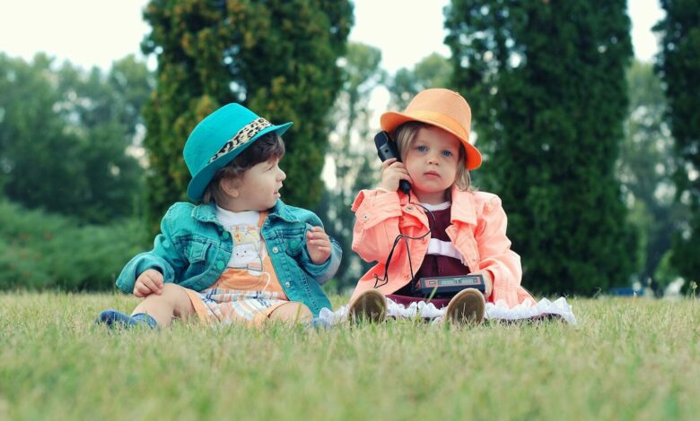 Two toddlers in colorful outfits enjoying playtime with walkie talkies in a sunny park setting.